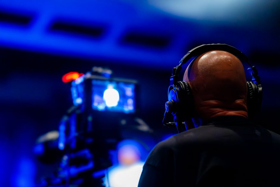Jornalismo Digital — A videographer wearing headphones captures an event with professional video equipment in a dimly lit